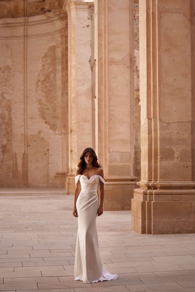 Timeless wedding gown crafted from lux Italian silk. It’s shaped with a gorgeous floor-length fitted draped by hand silhouette and delicate train. A heart-shaped neckline framed with wide V-straps.